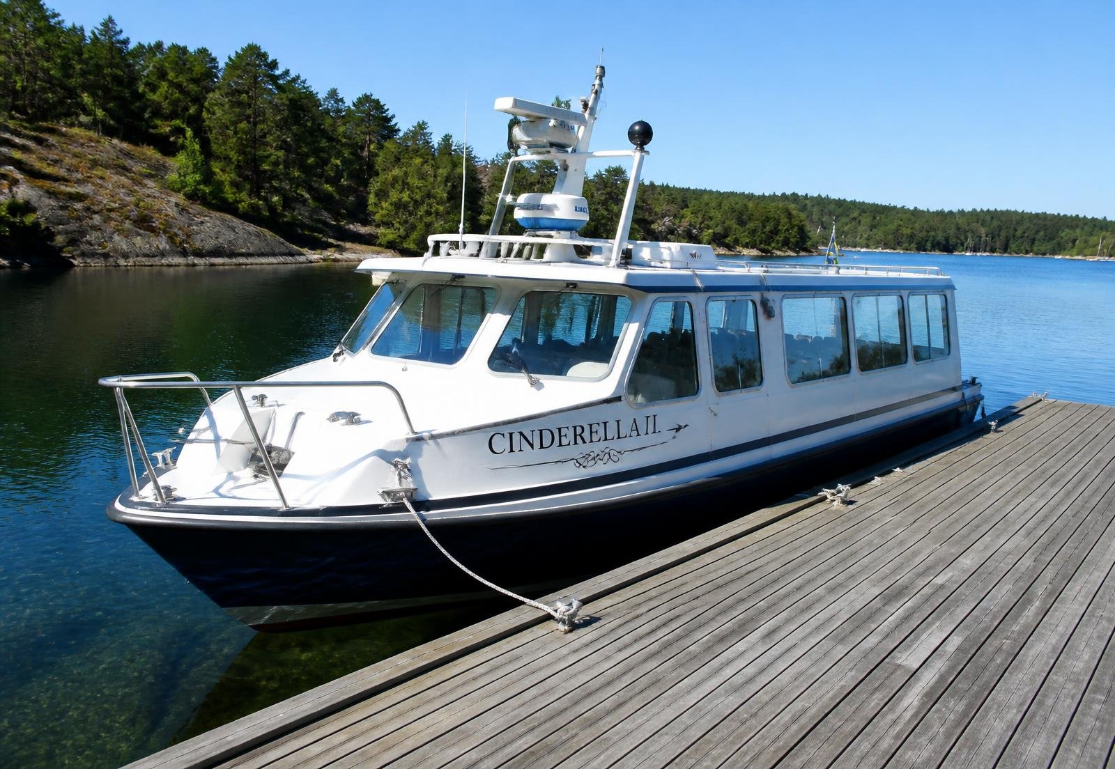 Vit passagerarbåt förtöjd vid brygga i svensk skärgård en sommardag